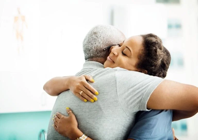 A side view of a female doctor hugging an older man in a clinic